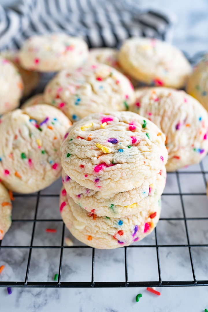 Sprinkle birthday cookies stacked on a wire cooling rack. 