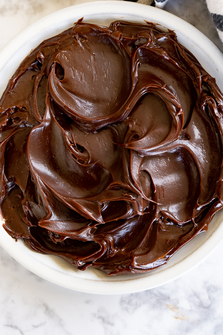A white heat-safe bowl filled with thick, shiny chocolate ganache.