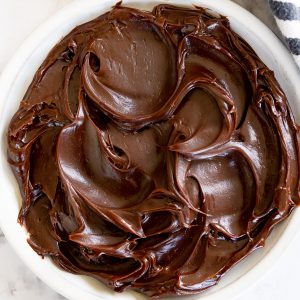 A white heat-safe bowl filled with thick, shiny chocolate ganache.