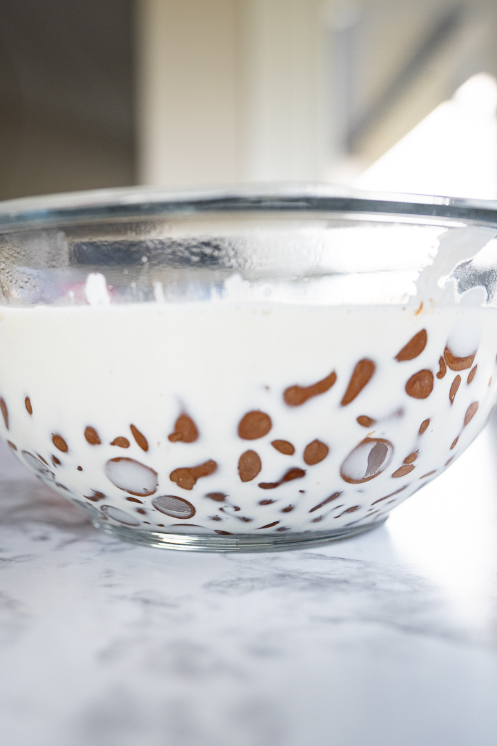 Side view of a glass bowl with chocolate chips and cream prior to being combined. 