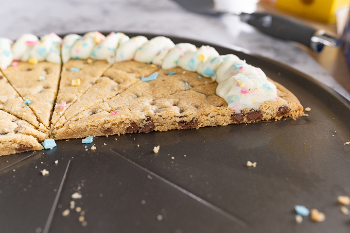Side view of a cookie pizza cut in half. Half of the pan is empty, while half remains. 