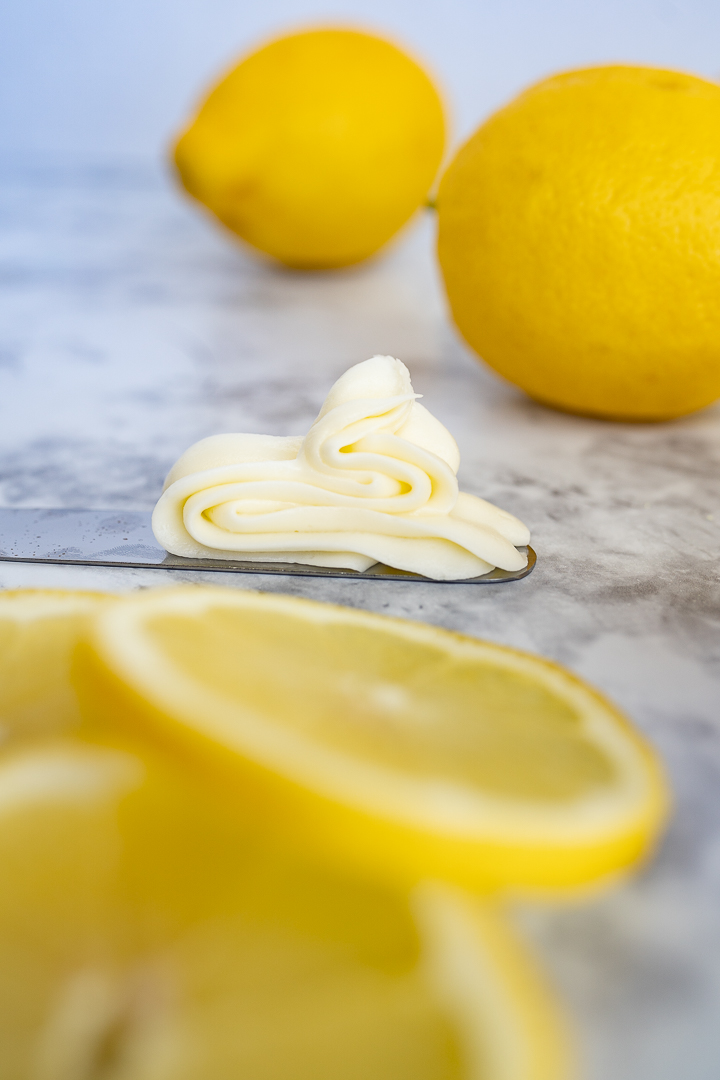 cream cheese lemon frosting piped on to a knife, laying in the middle of sliced and whole lemons. 