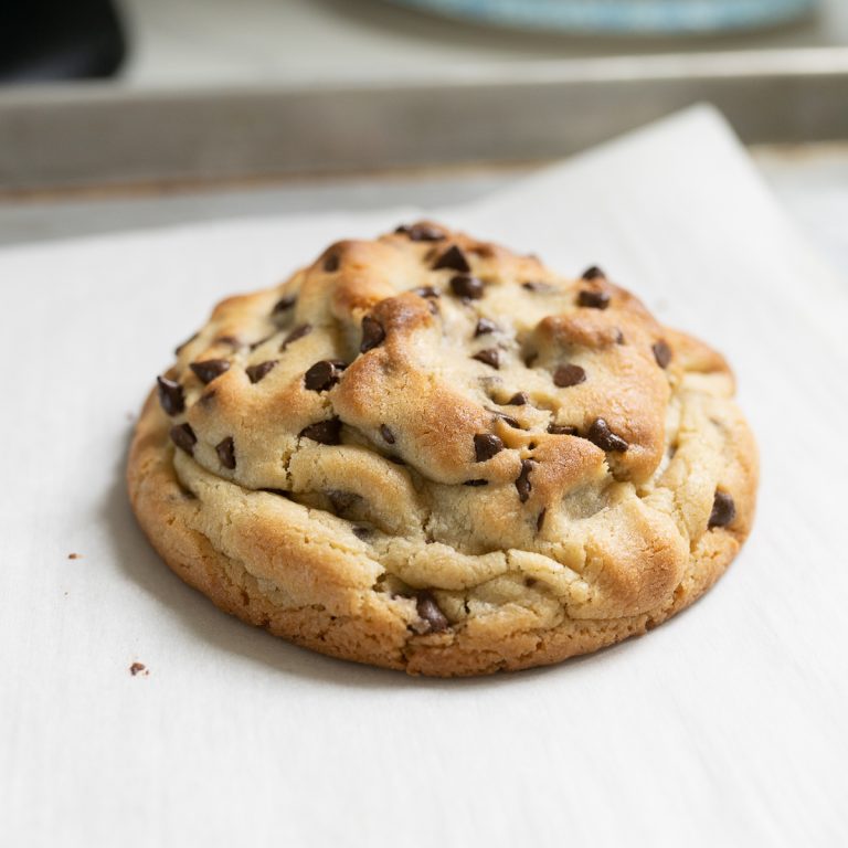 Single serve chocolate chip cookie sitting on a piece of parchment on the counter.