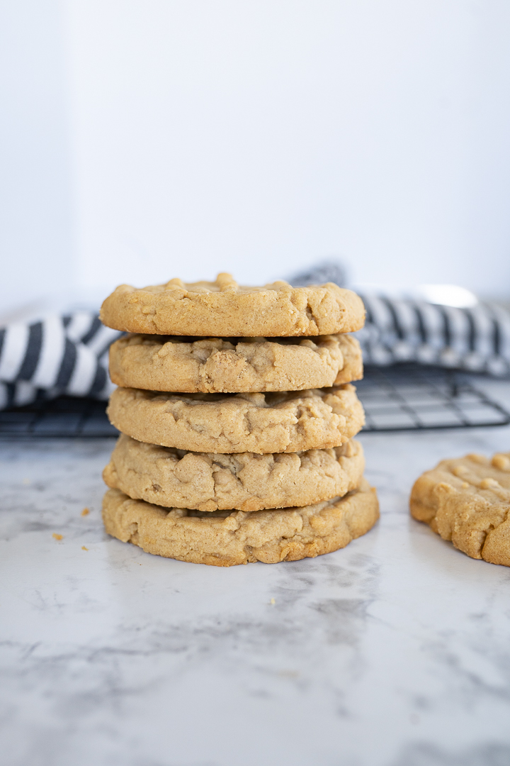 4 peanut butter cookies stacked on the counter. Next to the stack is a single cookie. 