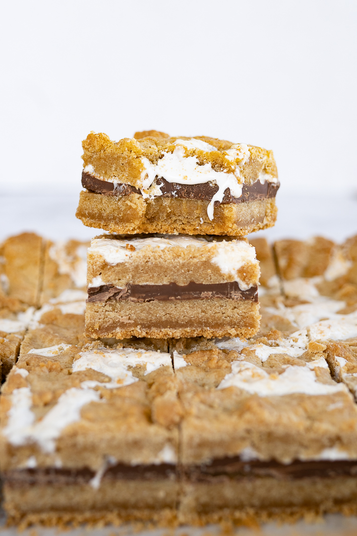 Two s'mores bar squares stacked on top of a sheet of bars. 