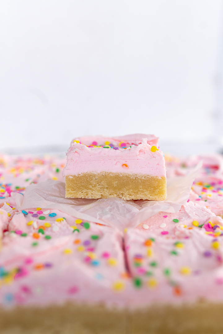 A side view of a single sugar cookie bar stacked on a plate of sugar cookie bars. 