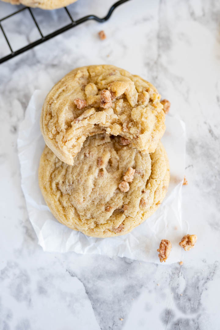 Two butter pecan cookies with sugared pecans stacked on the counter. One cookie has a bite out of it.