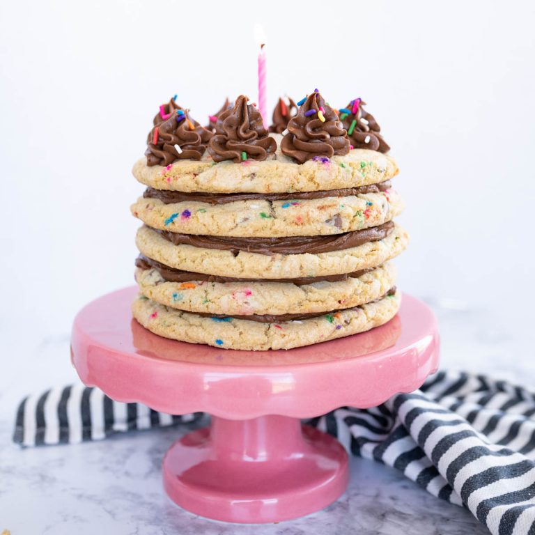 A cookie cake made of layered cookies and frosting on a pink cake stand.