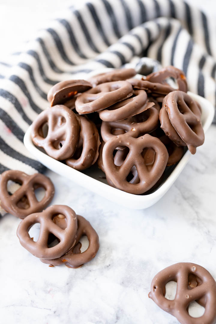 A bowl of chocolate covered pretzels sitting on a counter. Some pretzels have spilled out. 