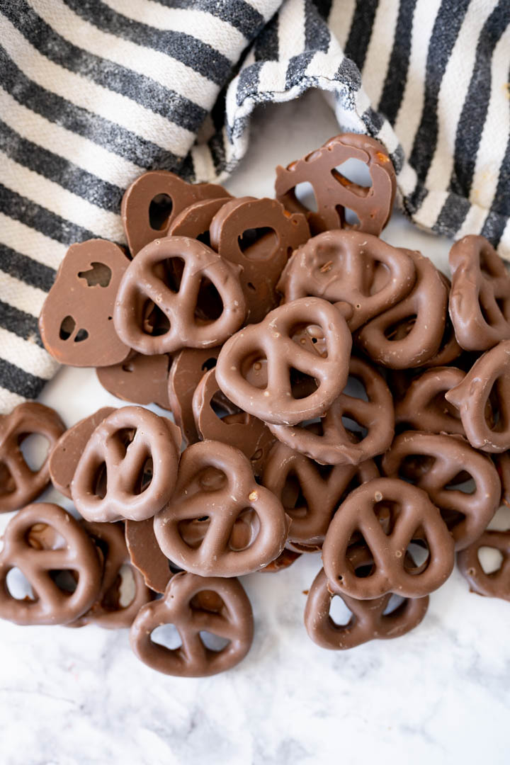 Newly chocolate covered pretzels spread on the counter next to a striped towel. 