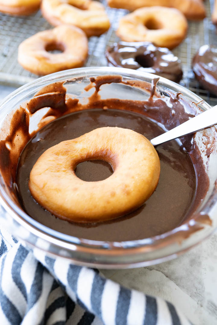A homemade donut being dipped in a bowl of chocolate glaze. 