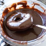 A homemade donut dipped in a bowl of chocolate glaze.