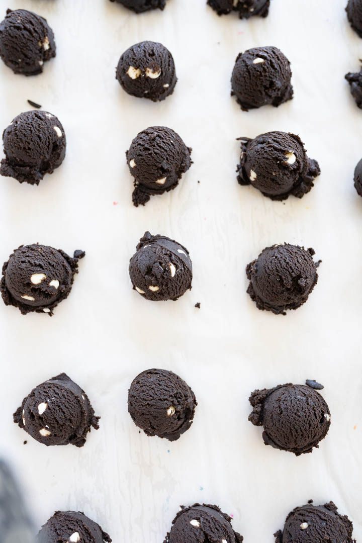 Chocolate crinkle cookie dough balls lined on a baking sheet ready to be rolled in powdered sugar. 