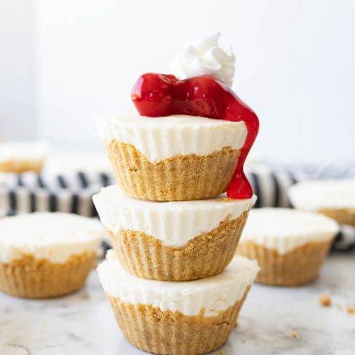 A stack of 3 mini cheesecakes topped with cherries and whipped cream.