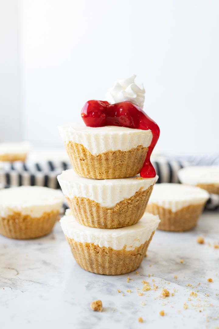 A stack of 3 mini cheesecakes topped with cherries and whipped cream.