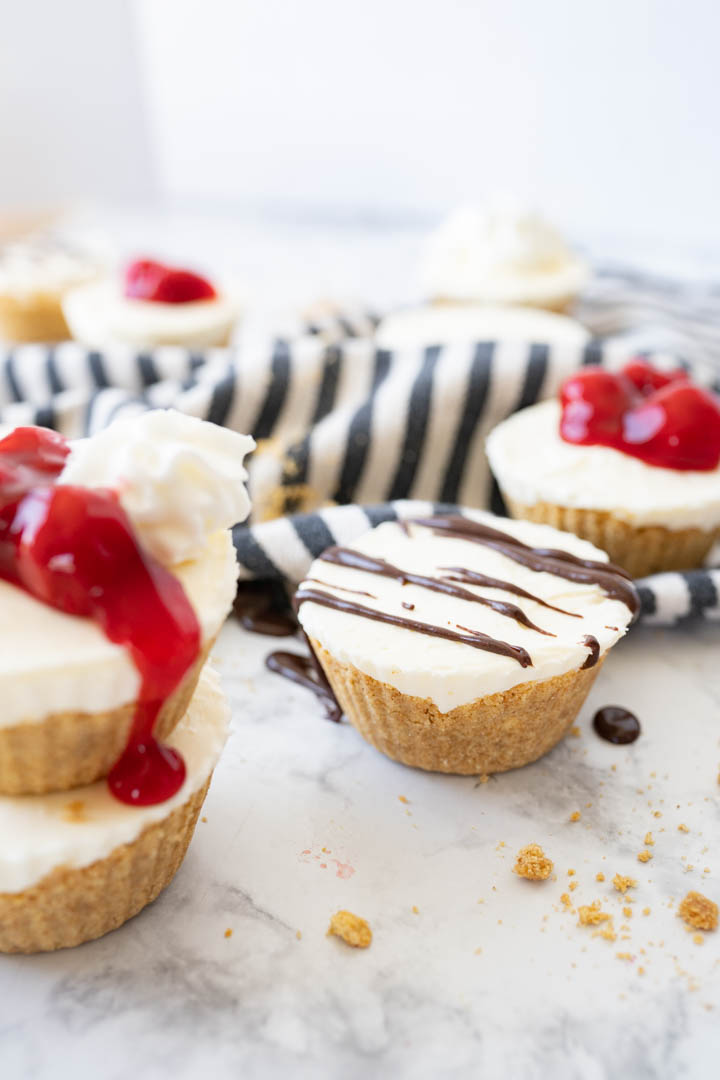 Mini cheesecakes topped with cherries and chocolate sauce sitting on a counter. 