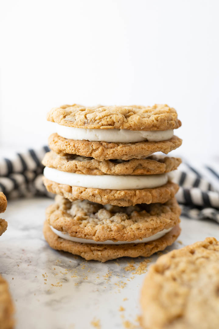 A stack of homemade oatmeal cream pie cookies on the counter next to a striped towel. 