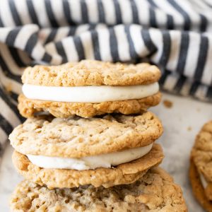 A stack of oatmeal cream pie cookies on a plate next to a striped towel.
