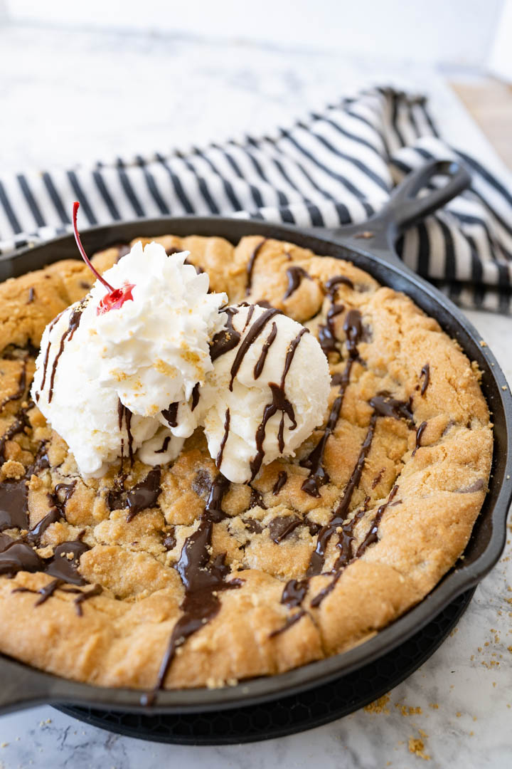 A freshly baked pizookie topped with ice cream and chocolate sauce. 