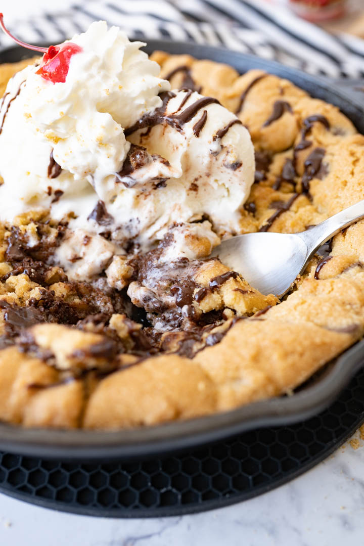 A gooey skillet cookie topped with ice cream. A spoon is sticking out of the partially eaten pizookie. 