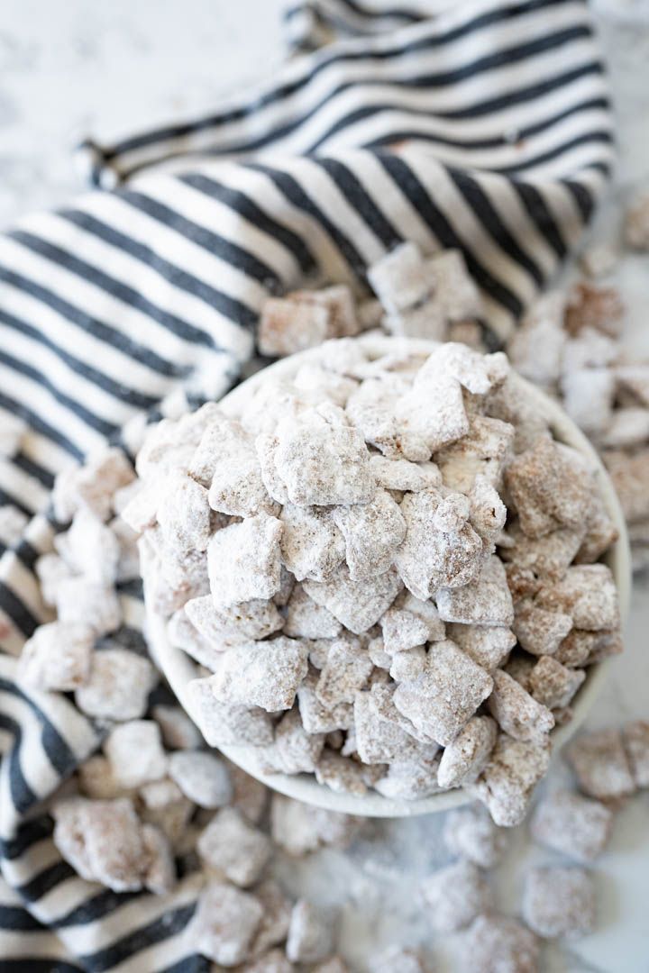 Aerial view of an overflowing bowl of puppy chow, spilling out onto a striped towel and the counter. 