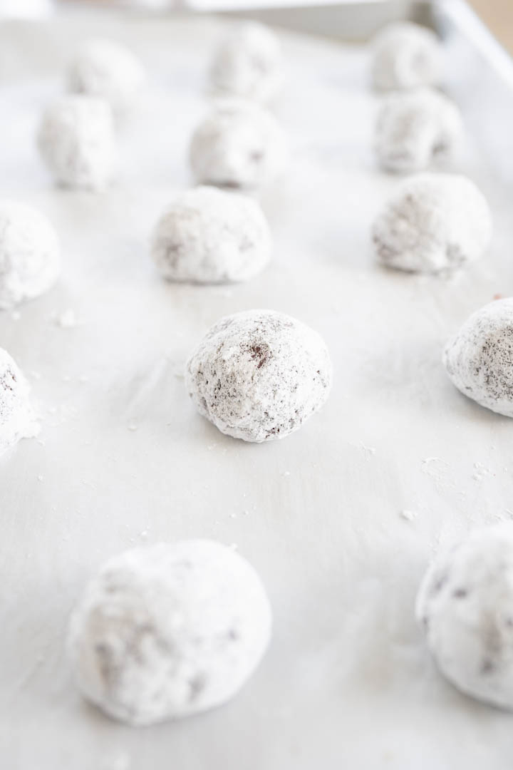 A sheet pan filled with red velvet cookie dough balls rolled in powdered sugar ready to be baked! 