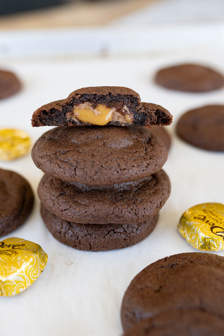 A stack of chocolate caramel cookies. The top cookie is cut in half with the caramel exposed. 