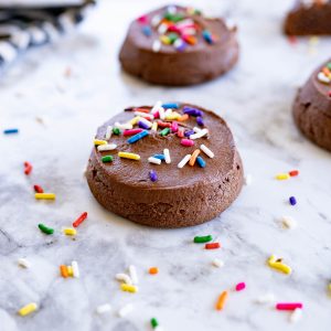 Side view of two chocolate lofthouse cookies on the counter with sprinkles around it.