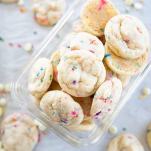 A container of white chocolate chip sprinkle cookies spilling out onto the counter.