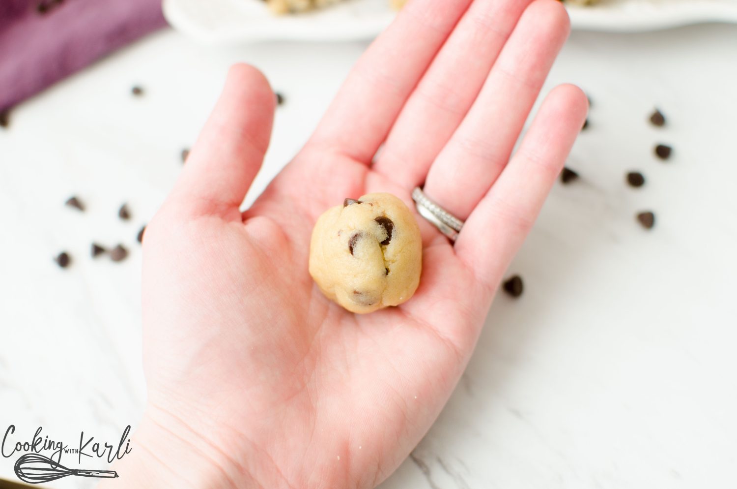 Edible chocolate chip cookie dough rolled into a ball and held in the palm of a hand. 