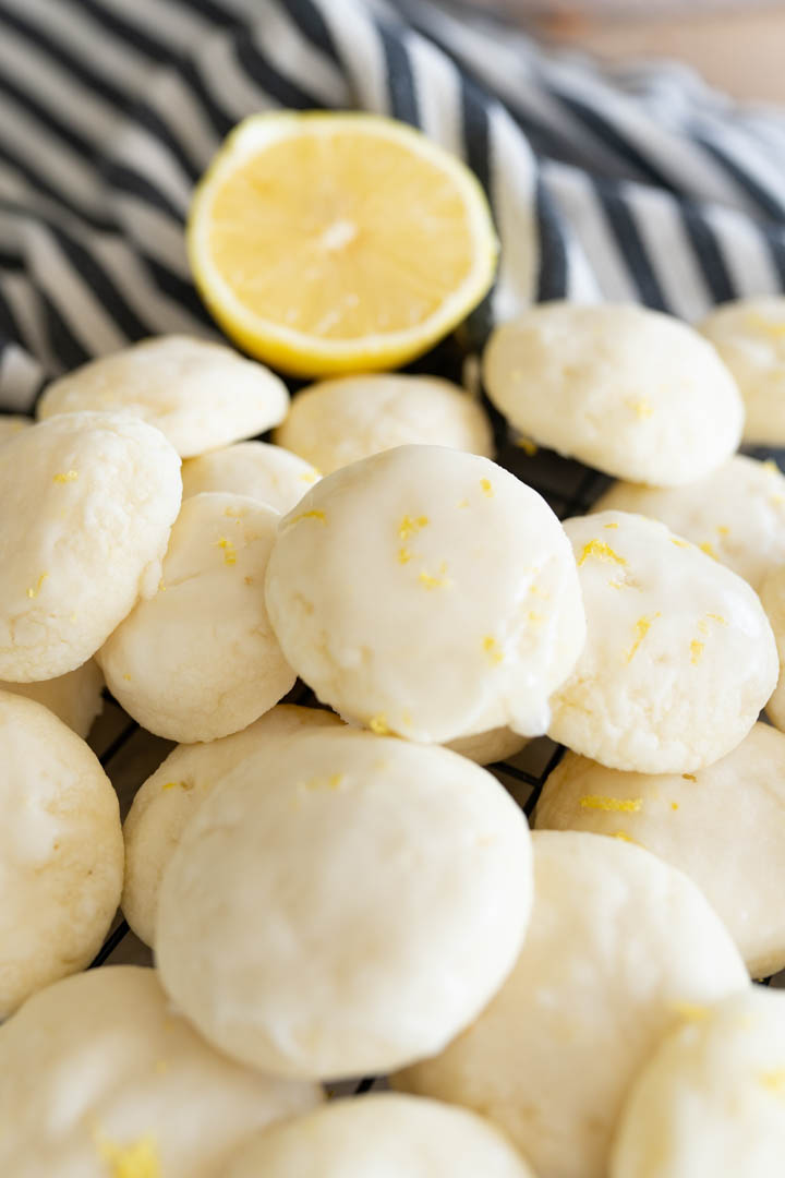 A pile of lemon meltaway cookies on the counter with a striped towel and a lemon slice. 