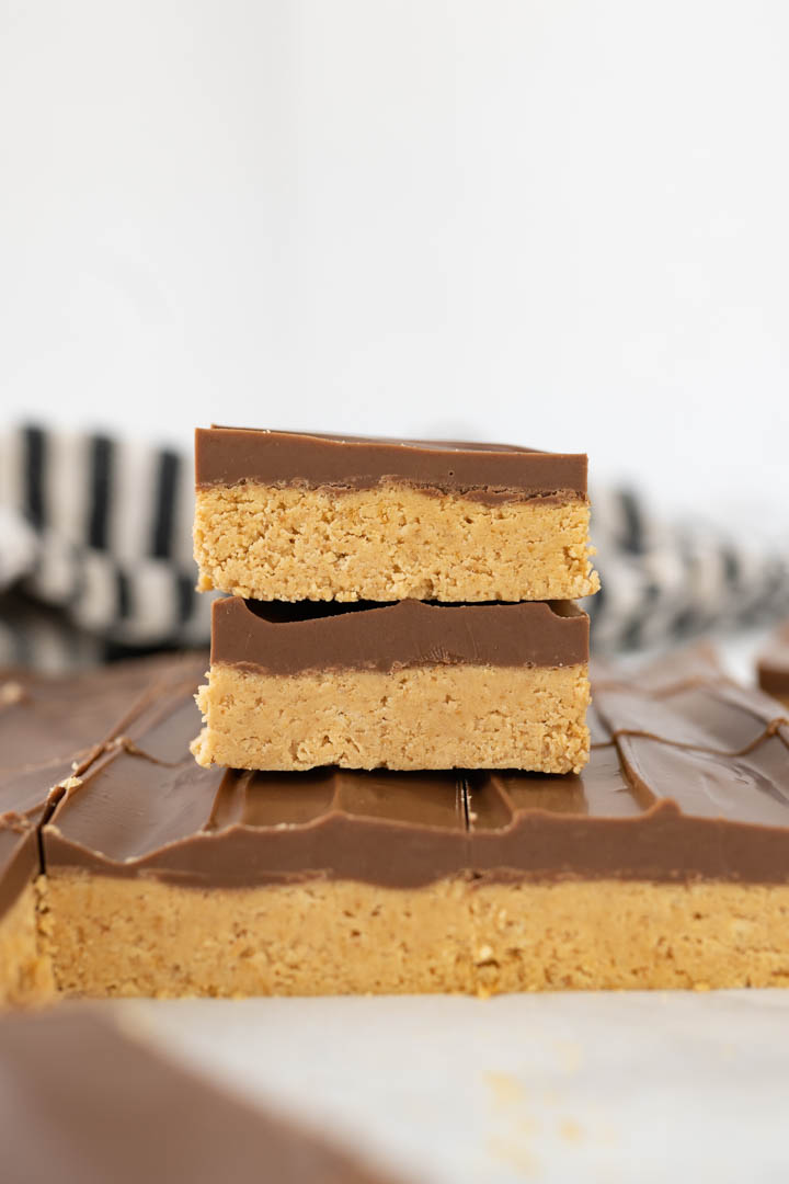 Two peanut butter bars stacked on top of a sheet of chocolate peanut butter bars. 