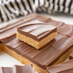 A peanut butter bar square stacked on top of a sheet of peanut butter bars.