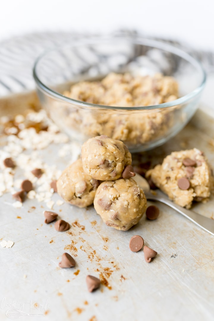 A bowl of edible oatmeal chocolate chip cookie dough, with a pile of edible cookie dough balls on the counter next to it. 
