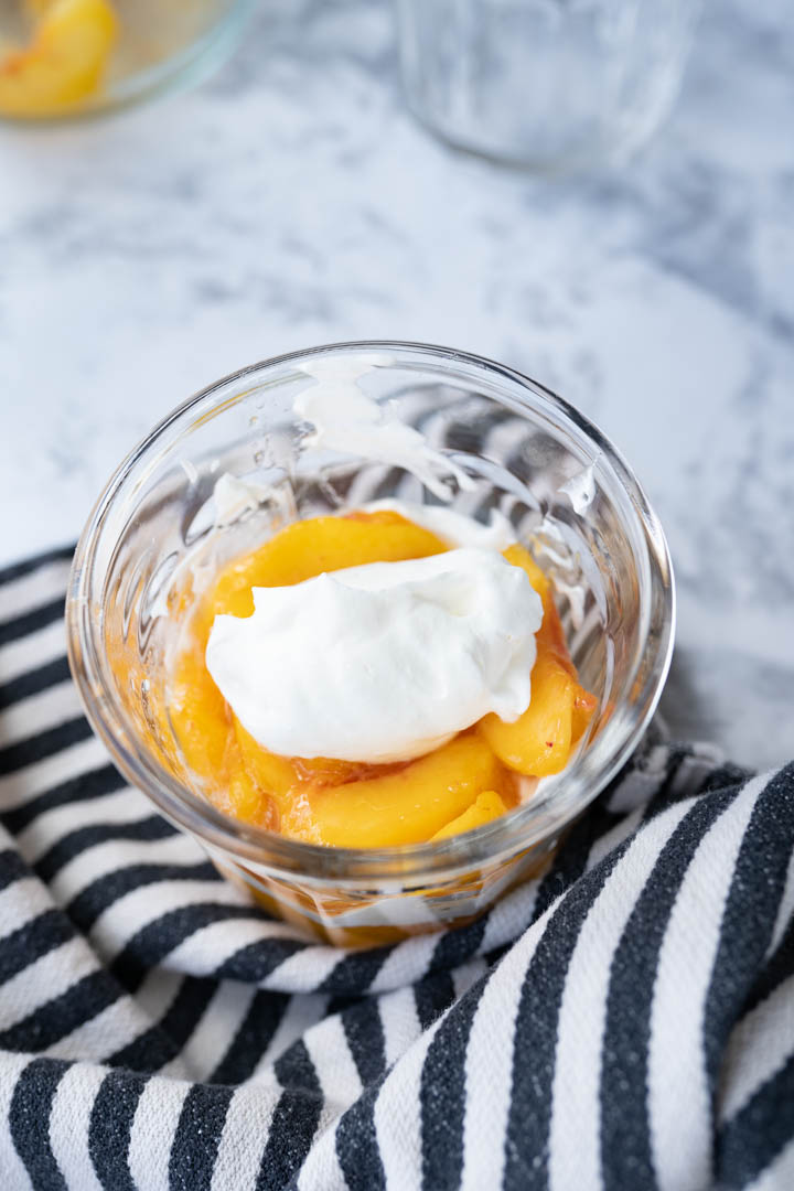 Aerial view of a glass filled with peaches and topped with a dollop of cream. 