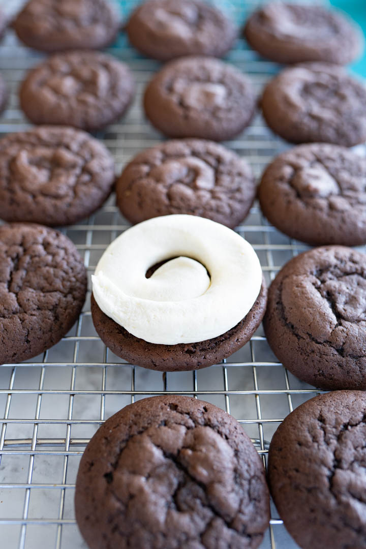 A tray of completed whoopie pie cookies with one cookie frosted without a top cookie. 