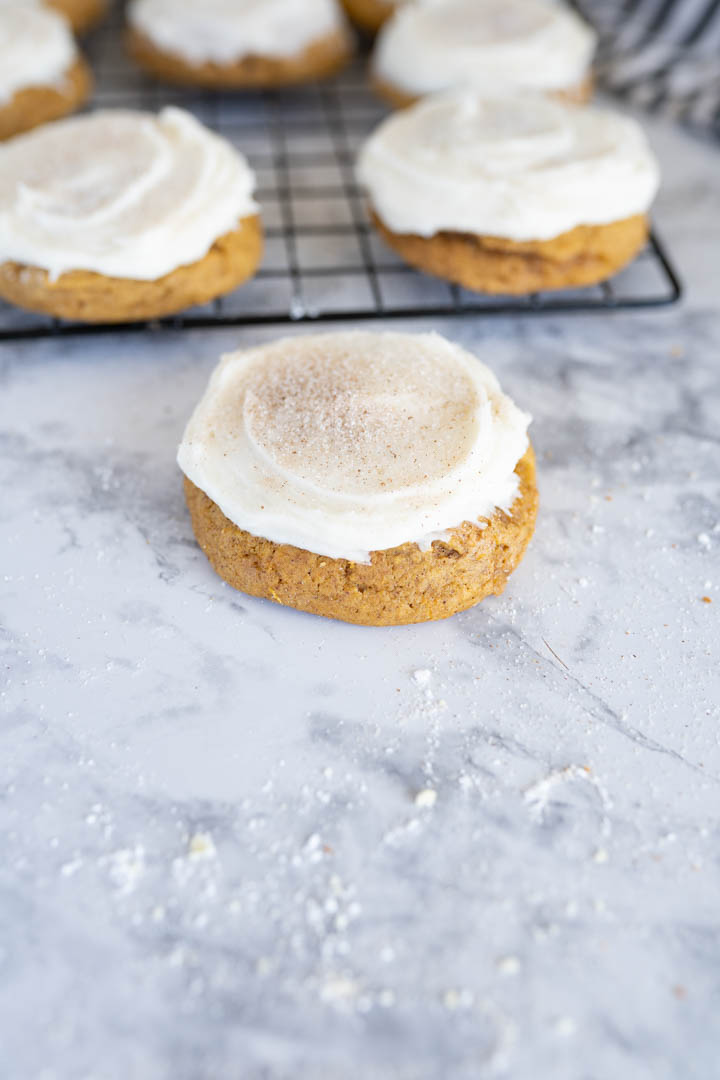 A single pumpkin cookie with cream cheese frosting on the counter. 