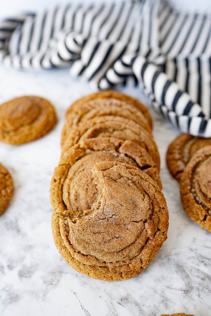 A horizontal stack of molasses cookies on the counter with a striped towel. 