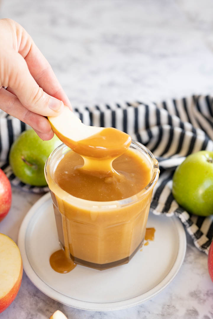 A hand pulling an apple slice out of caramel sauce. 