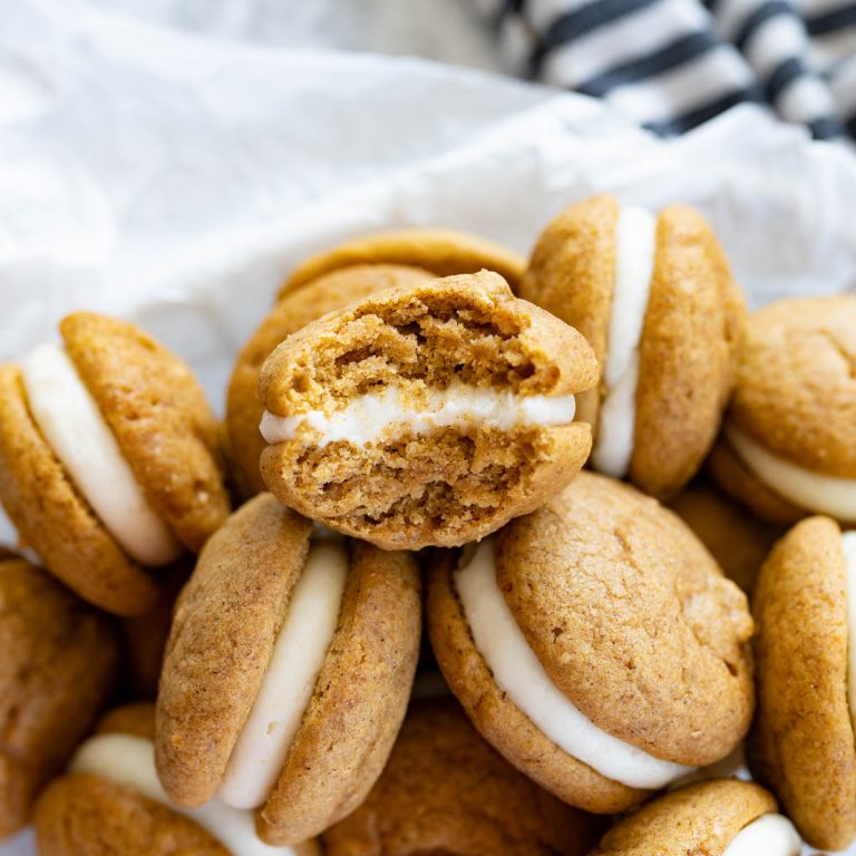 A pile of pumpkin whoopie pies. The one on top has a bite taken out of it.