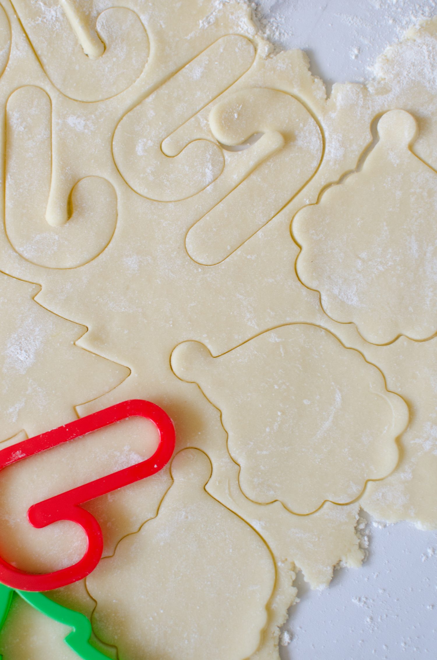 Christmas sugar cookie dough rolled out onto the counter with christmas cookies cut out of it. 