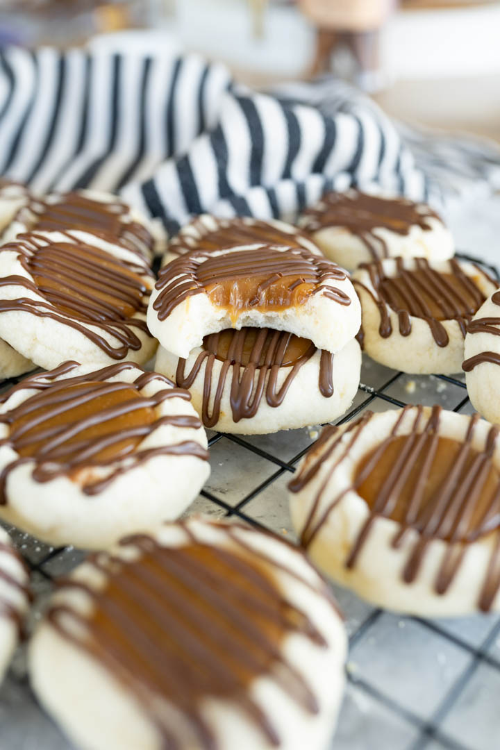 A pile of twix thumbprint cookies. On top there is a cookie with 1 bite out of it. 