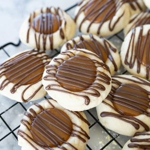 A pile of Twix Thumbprint cookies piled on a wire cooling rack.