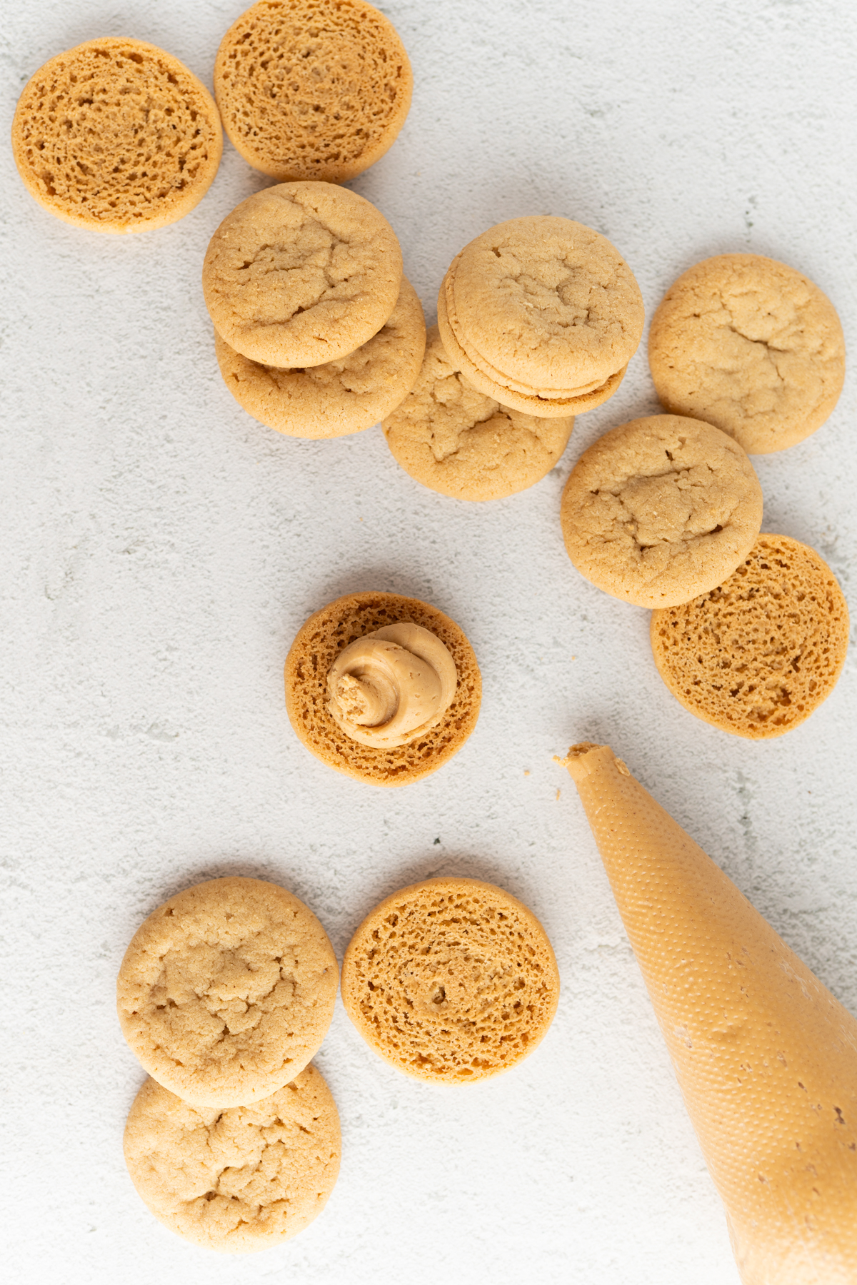 Aerial view of peanut butter cookies and a piping bag of peanut butter filling to make nutter butters. 