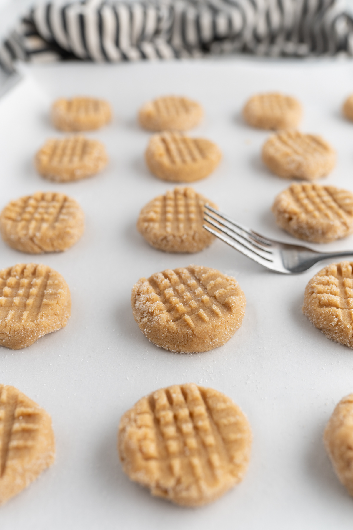 Peanut butter cookie dough pictured with a fork giving them the traditional criss cross pattern. 