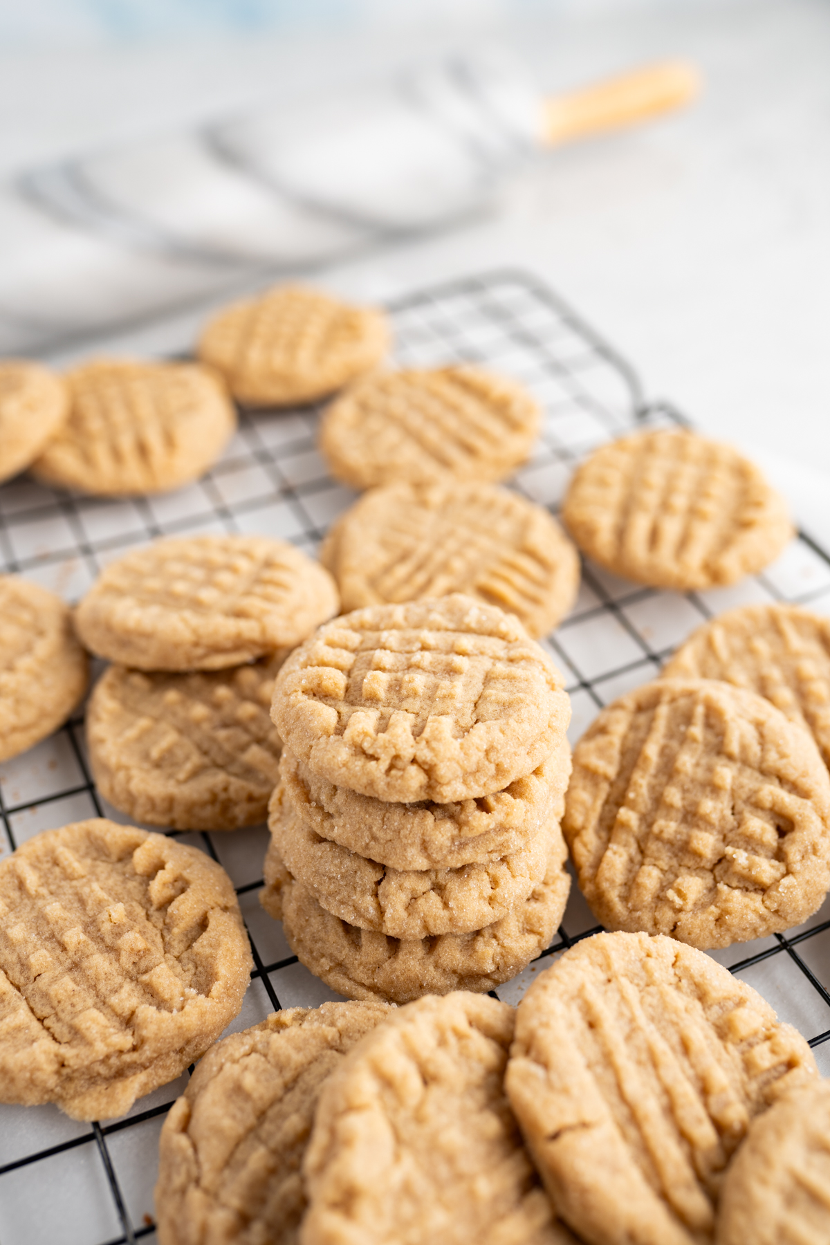 A stack of peanut butter cookies surrounded by scattered cookies on a wire cooling rack. 