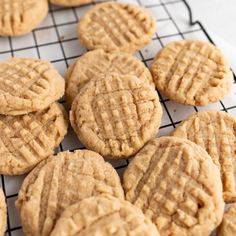 A pile of peanut butter cookies spread out on a wire cooling rack.