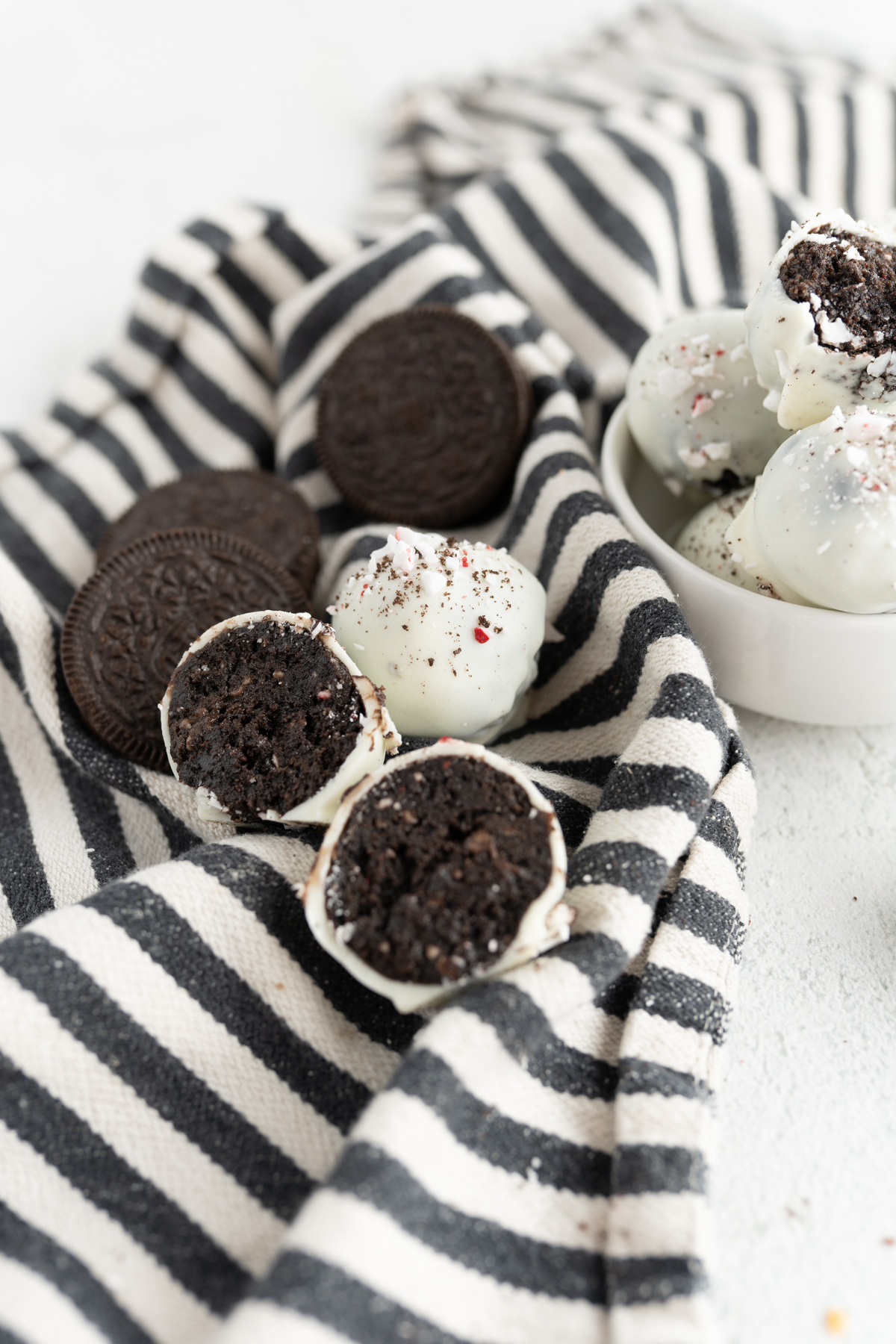 Peppermint oreo balls on a striped towel on the counter. One truffle is split in half. 