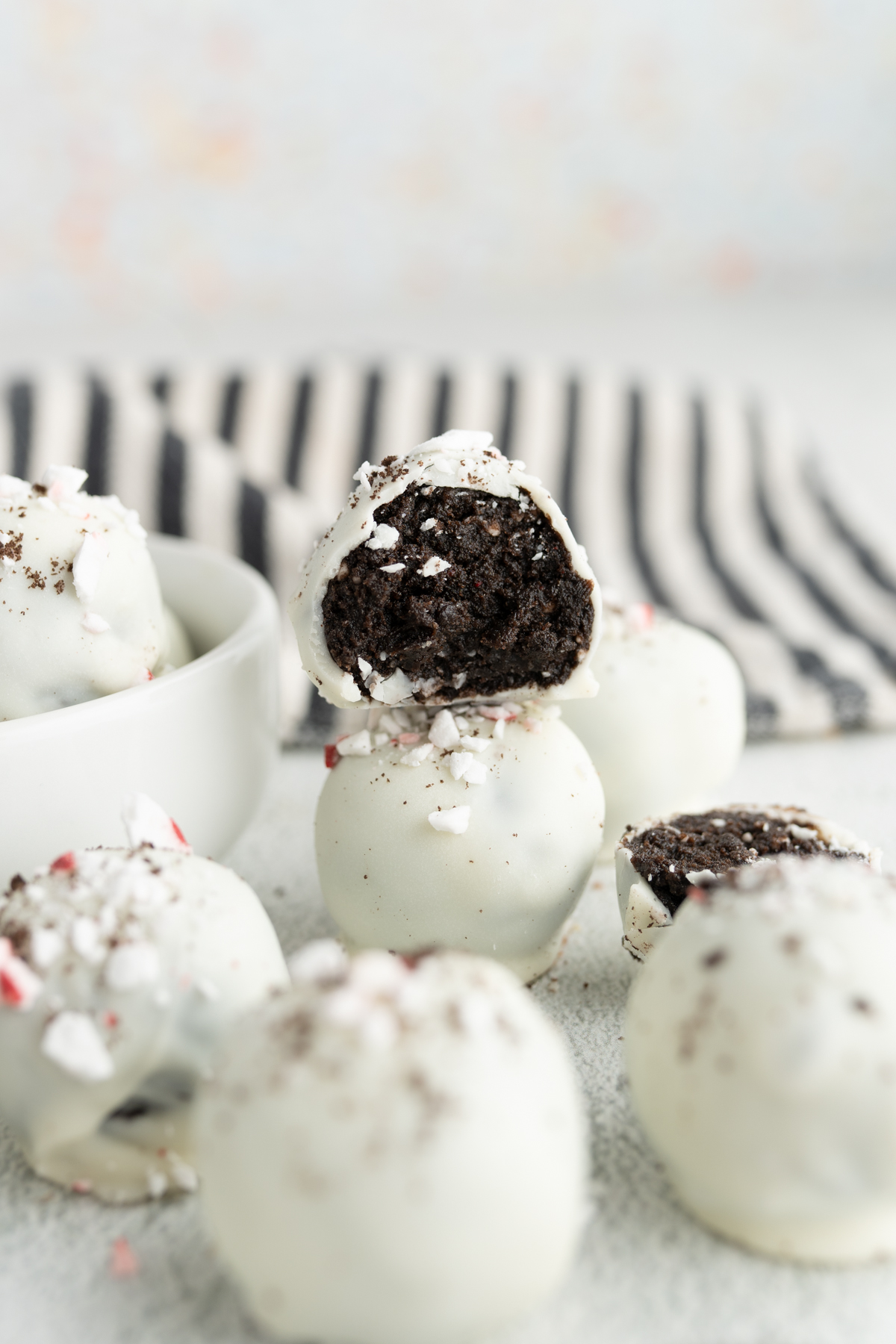 Peppermint oreo truffle balls on the counter. One truffle has a bite taken out of it and is stacked on top of a full one.