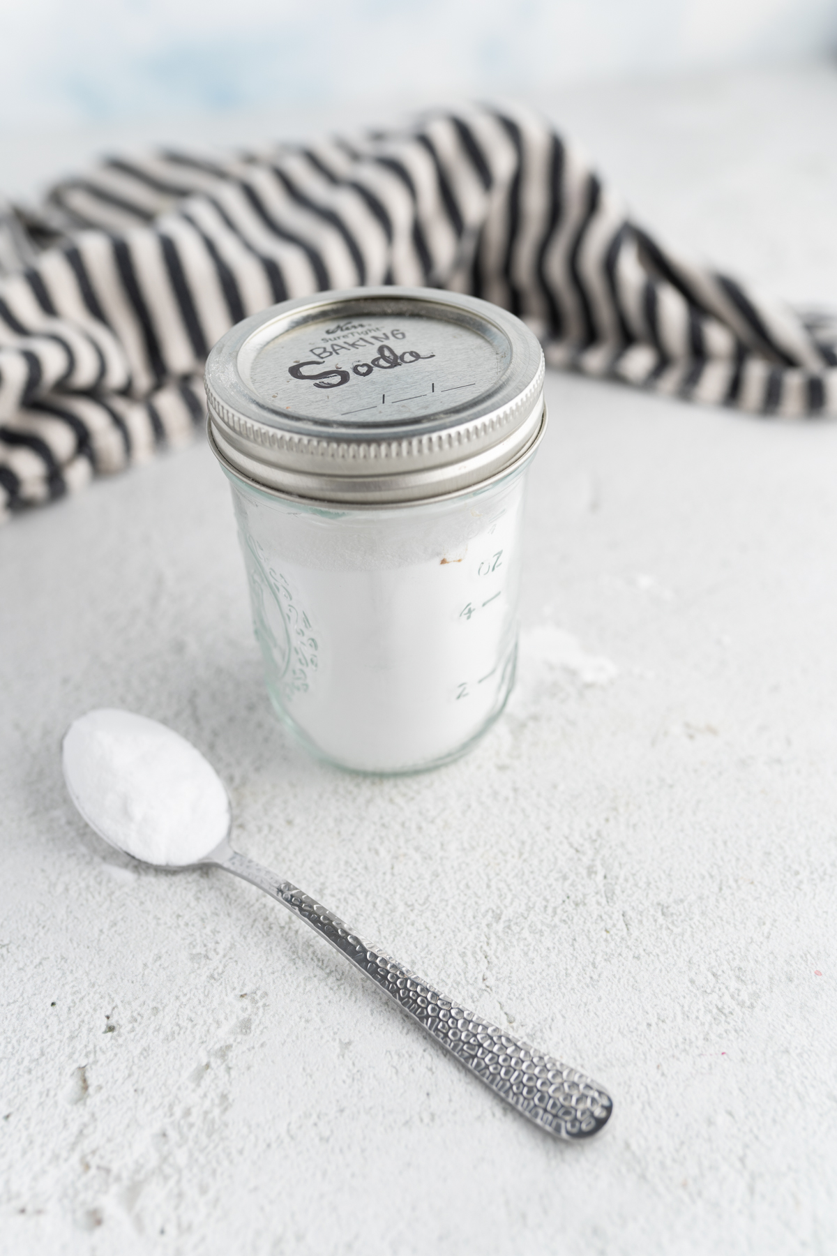 A mason jar labeled "baking soda" on the counter next to a spoonful of the substance. 
